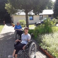 Mieszkańcy siedzący w wózkach inwalidzkich za pawilonem domu pomocy społecznej